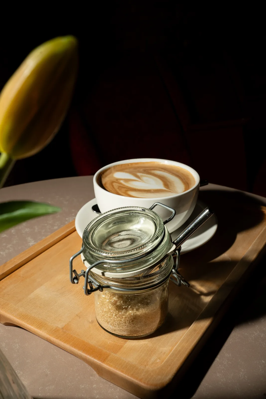 Cappuccino mit Latte Art auf einem Holzbrett neben einem Zuckerglas