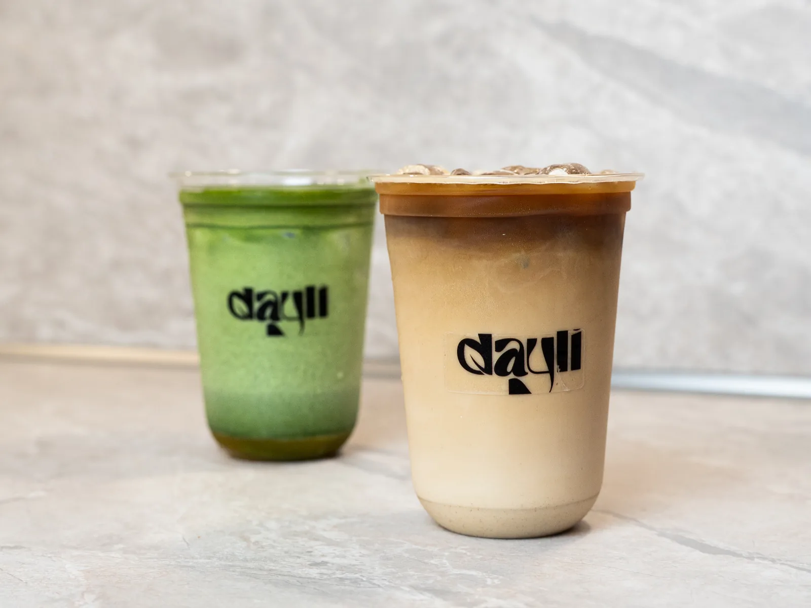 Iced Matcha und Iced Coffee im dayli-Becher auf hellem Steintisch
