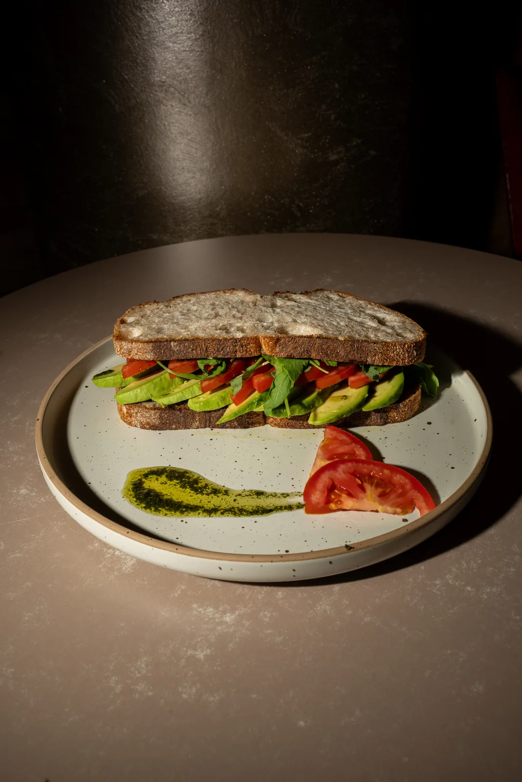 Avocado-Stulle mit Tomate, Rucola und Pesto auf einem Teller