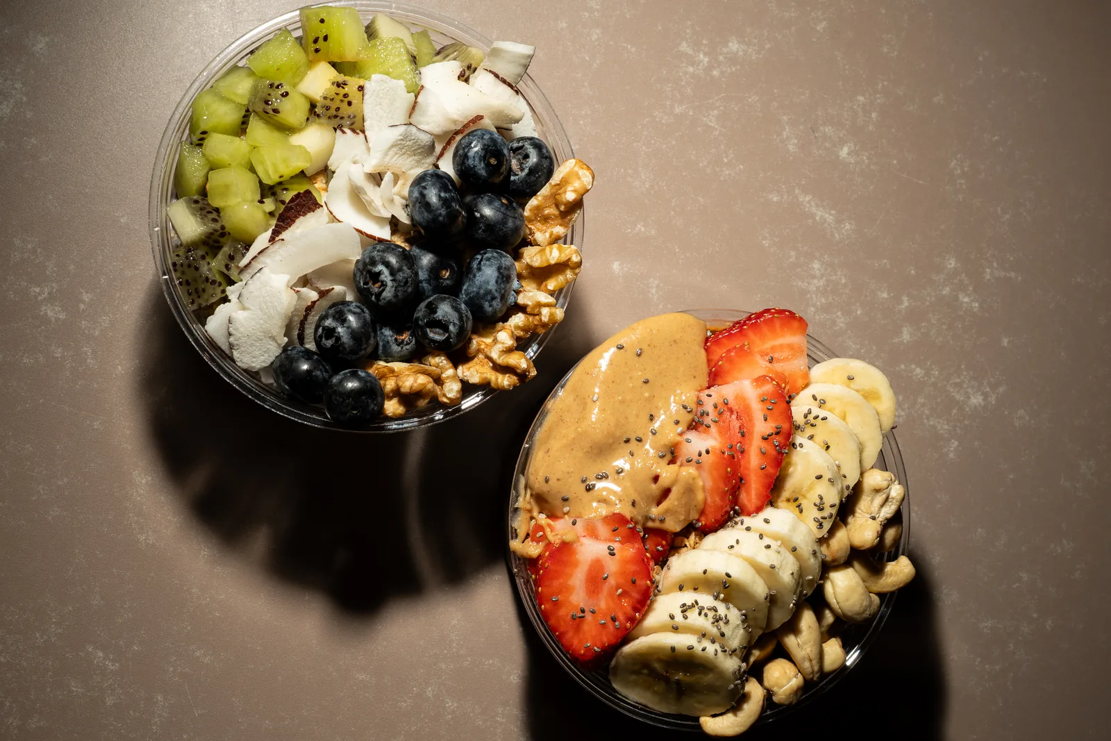 Zwei Bowls von oben: Kiwi, Kokos und Blaubeeren neben Erdbeere und Banane